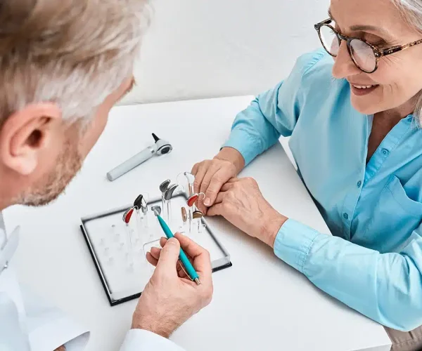 התאמת מכשירי שמיעה בבית הלקוח, מומחה שמיעה יושב ומסביר לגברת על מכשירי שמיעה